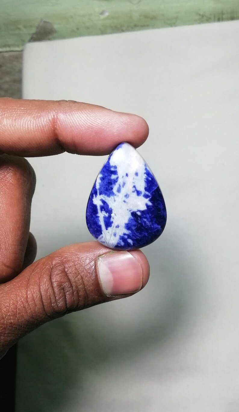 May include: A teardrop-shaped cabochon gemstone with a blue and white marbled pattern. The stone is polished and has a smooth surface.
