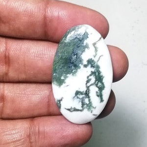 Puede incluir: Gema ovalada con base blanca y patrones intrincados verdes y azul oscuro. La piedra pulida se sostiene en una mano, mostrando su belleza natural. Ideal para la creación de joyas o coleccionismo.