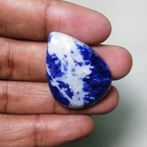 May include: A teardrop-shaped cabochon of blue and white sodalite. The stone has a swirling pattern of blue and white.