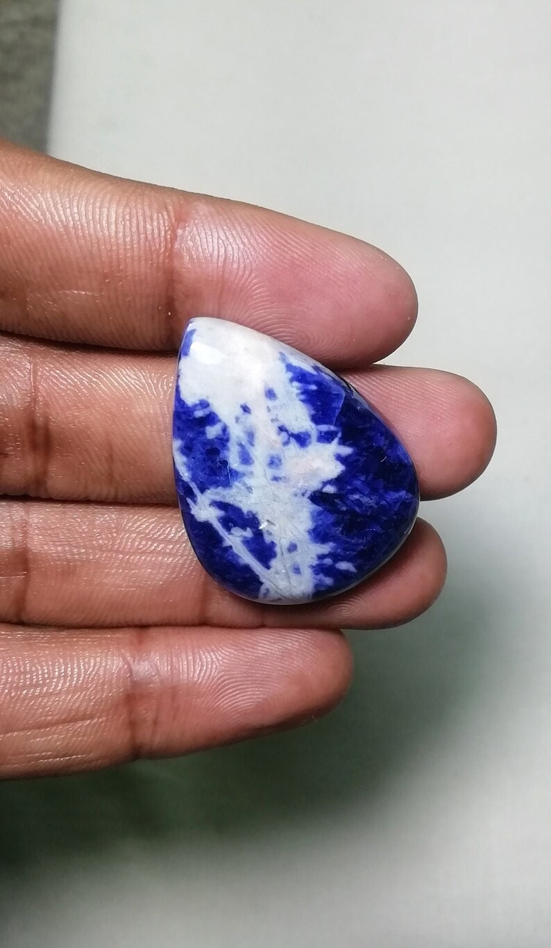 May include: A teardrop-shaped cabochon of blue and white sodalite. The stone has a swirling pattern of blue and white.