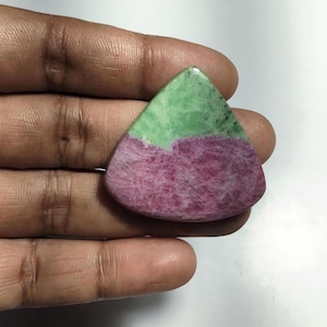 May include: A triangular-shaped polished gemstone featuring a distinct color split with a vibrant green upper section and a textured deep magenta lower section. The stone has a smooth, rounded edge and a flat surface, showcasing natural mineral patterns.
