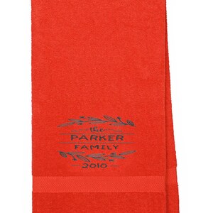 May include: Red bath towel with embroidered text "The Parker Family - 2010" in a black wreath design.