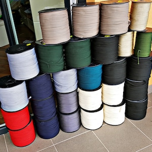 May include: A variety of spools of cord in different colors, including white, black, gray, blue, green, and red. The spools are arranged in a pyramid shape on a tiled floor.