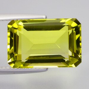 May include: A rectangular, faceted gemstone with a vibrant, translucent lime-yellow color. The stone features a classic emerald cut with sharp, clean edges and a highly reflective surface that catches light, displaying internal geometric facets.