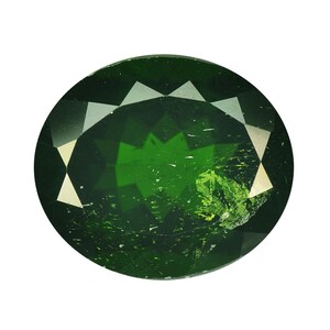 Puede incluir: Gema ovalada de color verde oscuro con facetas. La gema tiene una superficie pulida y un color vibrante, similar al esmeralda. Las facetas crean un juego de luces, realzando el brillo de la piedra. La gema está sobre un fondo blanco.