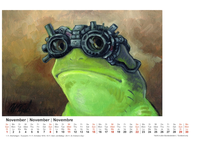 May include: A whimsical illustration of a green frog wearing steampunk goggles. The frog's face is centered, with the goggles prominently displayed. The background is a blend of brown and tan hues. A calendar for November is at the bottom.