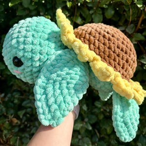 May include: A crocheted turtle toy with a brown shell and a yellow flower design. The turtle is green and has a cute face.
