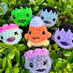 May include: Six crocheted Halloween-themed plush toys. The toys are in the shape of a monster, a candy corn, and a ghost. The toys are all different colors and have different facial expressions.