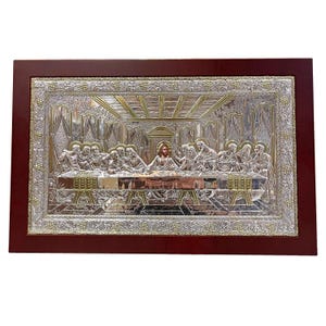 May include: A silver relief of the Last Supper, presented in a decorative frame. The artwork shows detailed figures and architectural elements, with a dark brown wooden frame.