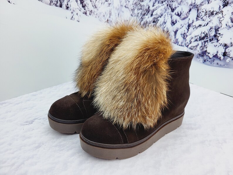 K&ouml;nnte beinhalten: Braune Wildlederstiefel mit dicker Plateau-Sohle und einem flauschigen Fuchs-Fellbesatz am oberen Rand des Stiefels.