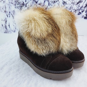 K&ouml;nnte beinhalten: Braune Wildleder-Keil-Stiefeletten mit einem Kunstfell-Besatz. Das Fell ist eine Mischung aus Braun und Wei&szlig;.