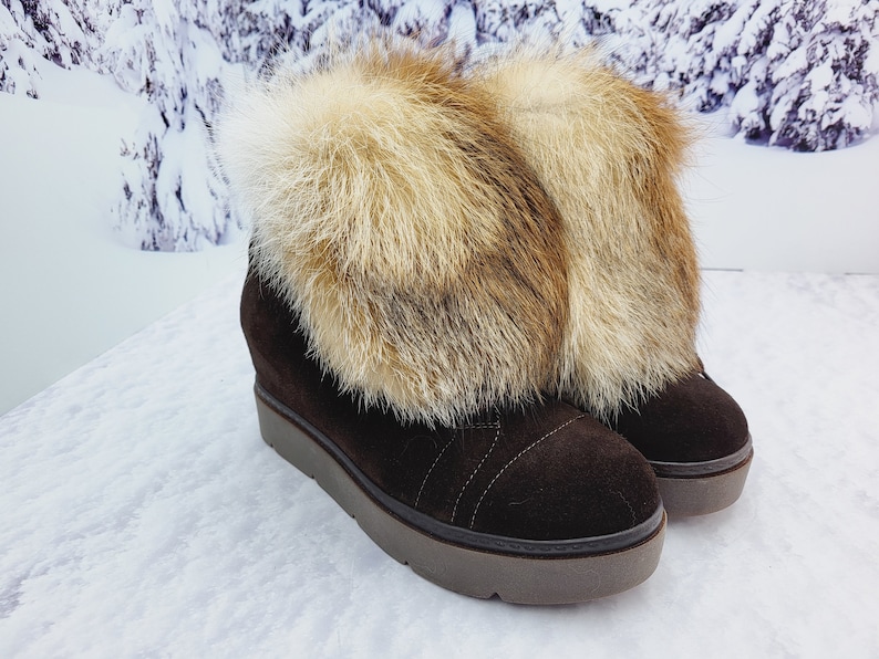 K&ouml;nnte beinhalten: Braune Wildleder-Keil-Stiefeletten mit einem Kunstfell-Besatz. Das Fell ist eine Mischung aus Braun und Wei&szlig;.
