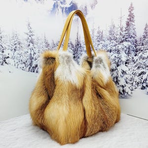 May include: A luxurious tote bag made of reddish-brown and white fur, with tan leather handles. The bag is fluffy and voluminous, perfect for carrying essentials. The background features a snowy winter scene.