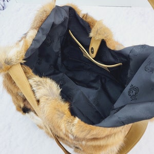 May include: A brown faux fur tote bag with a leather strap and a black fabric lining. The bag has a small interior pocket.