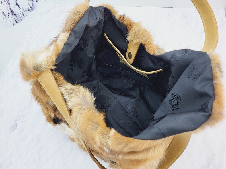 May include: A brown faux fur tote bag with a leather strap and a black fabric lining. The bag has a small interior pocket.