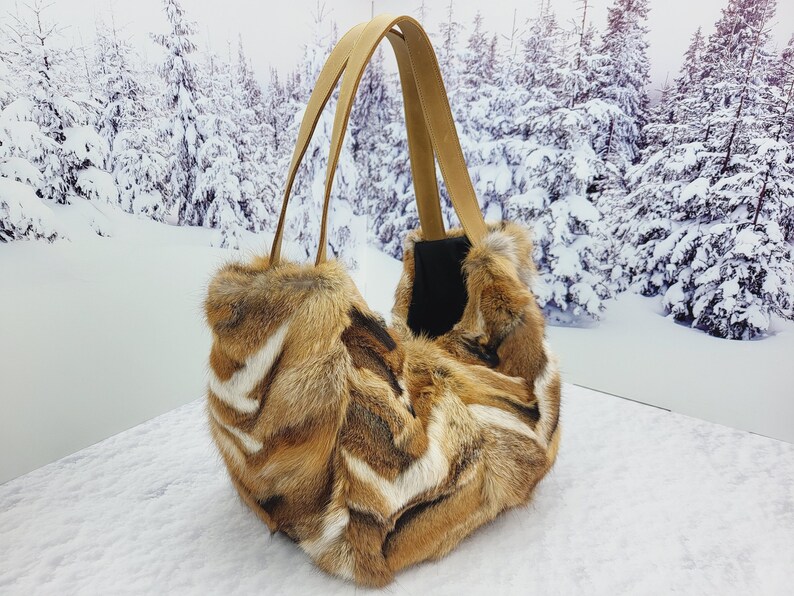 May include: A brown and white fur tote bag with leather straps. The bag is sitting on a snowy surface.