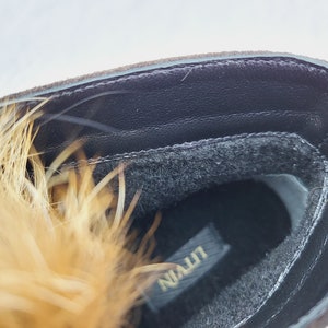 K&ouml;nnte beinhalten: Nahaufnahme des Innenraums eines braunen Wildlederstiefels mit schwarzem Pelzfutter. Der Stiefel hat eine schwarze Ledersohle mit dem in Gold gedruckten Wort "NIALLT".