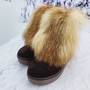 K&ouml;nnte beinhalten: Ein Paar braune Wildlederstiefel mit dicker Sohle und einem flauschigen braunen und wei&szlig;en Pelzbesatz am oberen Rand.
