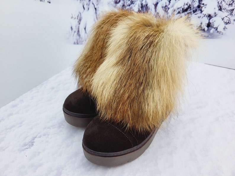 K&ouml;nnte beinhalten: Ein Paar braune Wildlederstiefel mit dicker Sohle und einem flauschigen braunen und wei&szlig;en Pelzbesatz am oberen Rand.