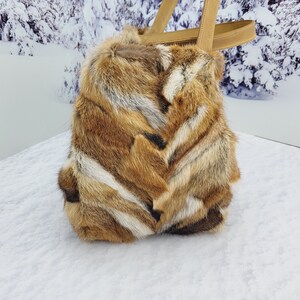 May include: A brown and white fur tote bag with leather handles. The bag is sitting on a snowy surface.