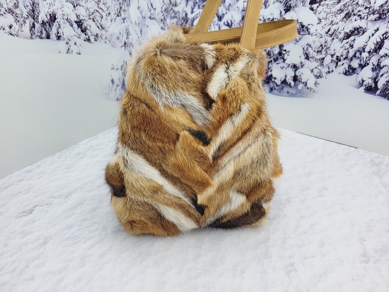 May include: A brown and white fur tote bag with leather handles. The bag is sitting on a snowy surface.