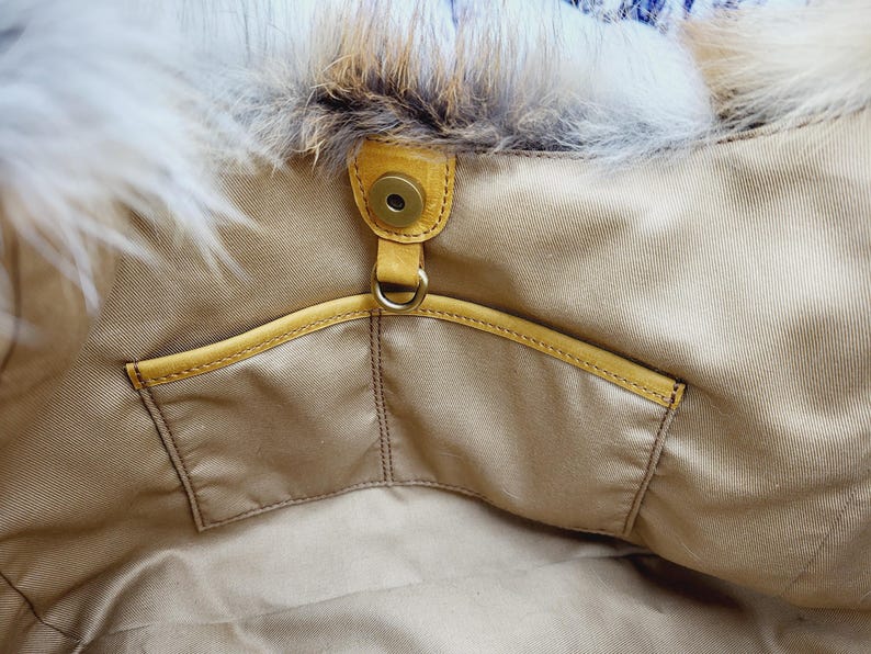 May include: Close-up of a beige handbag interior with a yellow leather pocket and trim. The bag features a magnetic snap closure and a fluffy, white and brown fur trim along the top edge. The bag's interior is a light beige fabric.