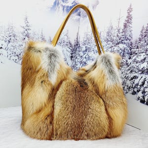 May include: A large, rectangular handbag made of brown and tan fur with a light brown leather handle. The bag is set against a backdrop of a snowy forest scene.