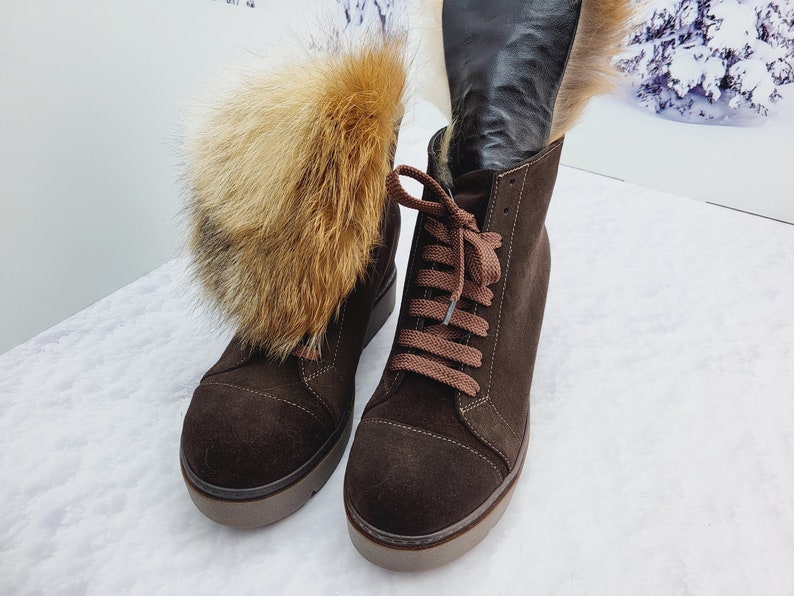 K&ouml;nnte beinhalten: Ein Paar braune Wildlederstiefel mit Pelzbesatz. Die Stiefel haben Schn&uuml;rsenkel und eine dicke Plateau-Sohle.