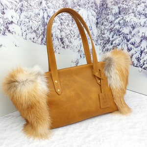 May include: A brown leather tote bag with fox fur trim. The bag has two top handles and a zipper closure.