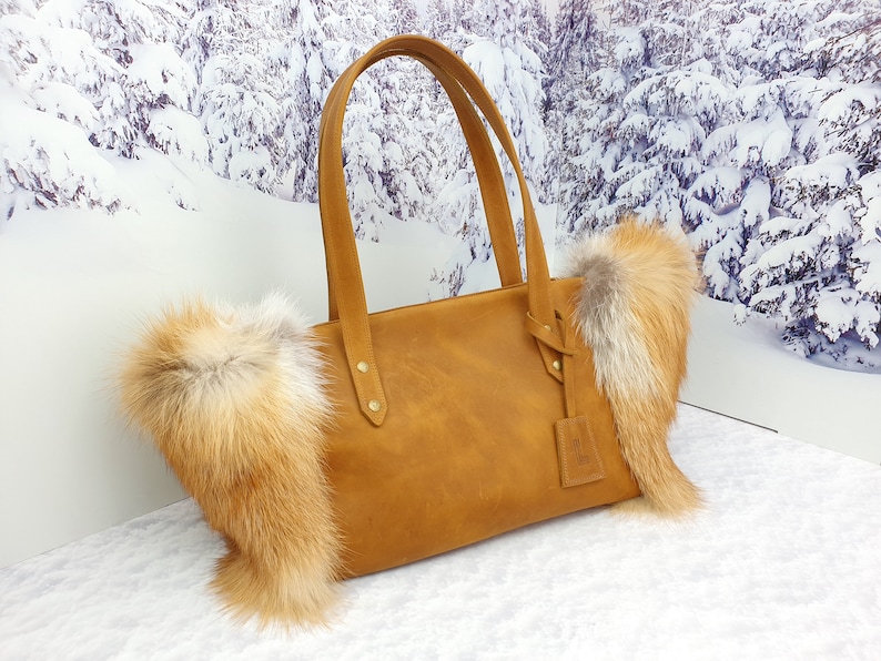May include: A brown leather tote bag with fox fur trim. The bag has two top handles and a zipper closure.