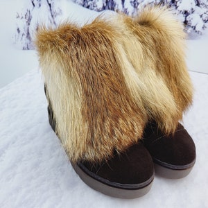 K&ouml;nnte beinhalten: Ein Paar braune Wildlederstiefel mit einem Kunstfellbesatz. Das Fell ist eine Mischung aus Braun und Blond.