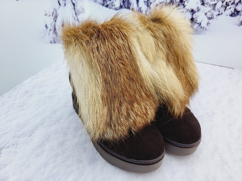 K&ouml;nnte beinhalten: Ein Paar braune Wildlederstiefel mit einem Kunstfellbesatz. Das Fell ist eine Mischung aus Braun und Blond.