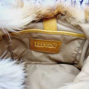 May include: Interior view of a tan handbag with a fur trim. The bag features a leather label with the embossed word "LITVIN". The bag's interior is visible, showing a pocket and a leather strap.