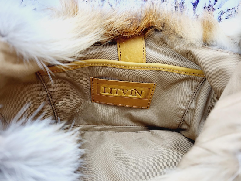May include: Interior view of a tan handbag with a fur trim. The bag features a leather label with the embossed word "LITVIN". The bag's interior is visible, showing a pocket and a leather strap.