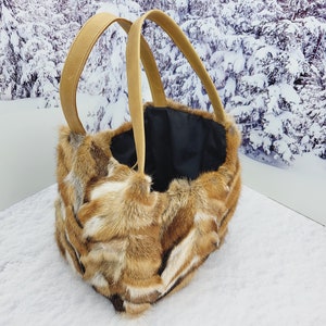 May include: A brown and white fur tote bag with leather handles. The bag is sitting on a white surface.
