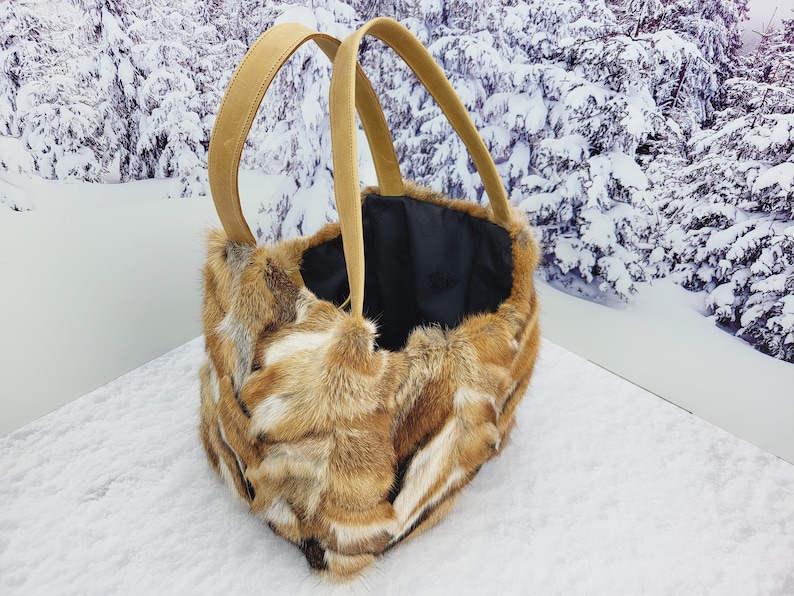 May include: A brown and white fur tote bag with leather handles. The bag is sitting on a white surface.