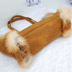 May include: A brown leather tote bag with fox fur trim. The bag has two straps and a top zipper closure.