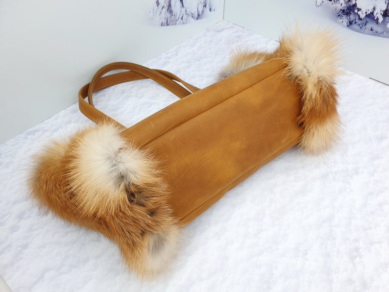 May include: A brown leather tote bag with fox fur trim. The bag has two straps and a top zipper closure.