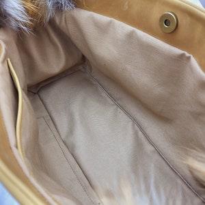 May include: The inside of a light brown leather tote bag with a zippered pocket and a fur trim. The bag is lined with a light beige fabric.