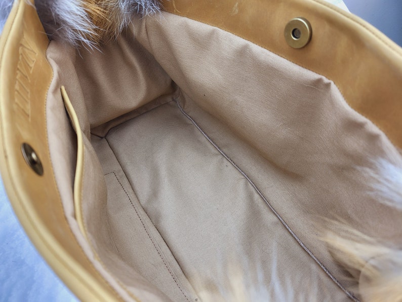 May include: The inside of a light brown leather tote bag with a zippered pocket and a fur trim. The bag is lined with a light beige fabric.