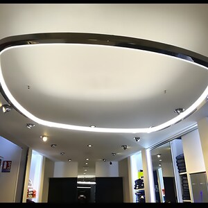 Peut inclure: Un plafond blanc moderne avec un grand luminaire incurvé chromé. Le luminaire est en forme d'anneau avec une source de lumière blanche.