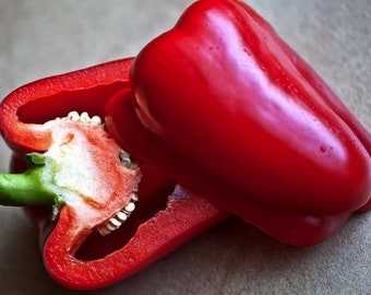 May include: A red bell pepper cut in half, showing the inside with seeds. The other half of the pepper is still whole.