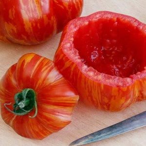 May include: Three red and yellow striped tomatoes, one of which has been cut open to reveal the red flesh inside. A silver knife is lying on the wooden surface.