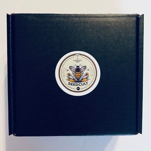 May include: A black cardboard box with a round sticker featuring a bee illustration and the text "SEEDCULT" in white lettering.