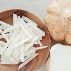 K&ouml;nnte beinhalten: Eine Holzschale gef&uuml;llt mit wei&szlig;en, julienne-geschnittenen Jicama. Neben der Schale befinden sich eine ganze Jicama und ein St&uuml;ck Jicama. Die Jicama hat eine hellbraune Schale und ein wei&szlig;es Inneres. Die Schale ist rund und aus Holz.