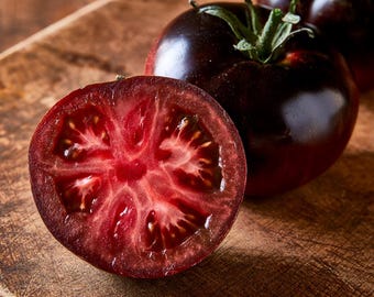 May include: A whole dark purple tomato with a green stem and a sliced half tomato showing a vibrant red interior with visible seeds and pulp. The tomatoes have a smooth, glossy skin and are positioned to display both the exterior and interior.