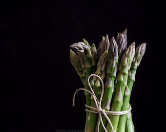 May include: A bunch of fresh green asparagus spears tied together with twine. The asparagus is arranged in a circular shape, with the tips of the spears pointing upwards.