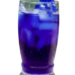 May include: A tall glass filled with a vibrant blue beverage, ice cubes, and garnished with blue flowers and green leaves. The drink appears refreshing and is set against a white background.