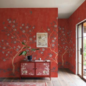 Può includere: Una stanza con pareti rosse con un design ad albero floreale. Un mobile rosso con accenti floreali si trova sotto un quadro incorniciato. Sono visibili anche una pianta in vaso e un tappeto. La stanza ha un pavimento in legno e una porta verso l'esterno.