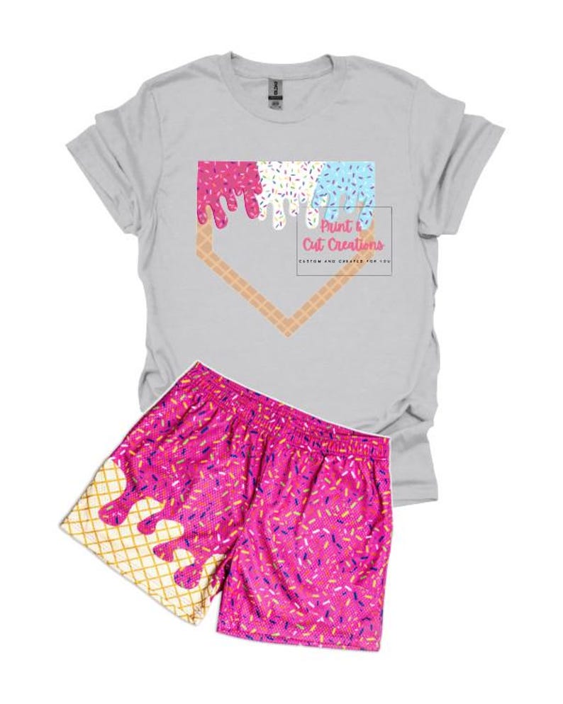 May include: A gray t-shirt with a pink, blue, and white ice cream cone graphic in the shape of a baseball diamond. The text "Print & Cut Creations" is below the graphic. A pair of pink athletic shorts with a matching ice cream cone graphic.